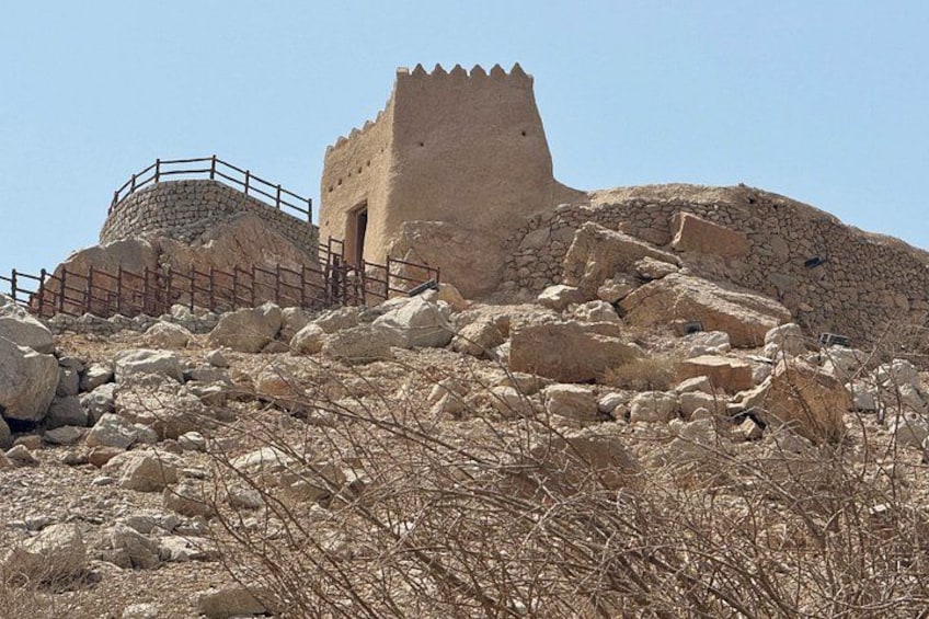 A historical stone structure with a tower, surrounded by rocky terrain and sparse vegetation. 4