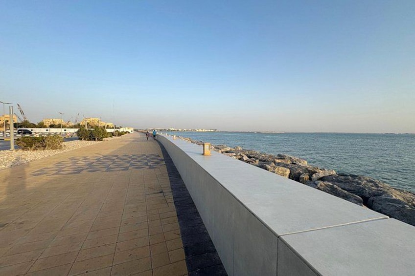 A coastal walkway with a paved path, a low wall, and a rocky shoreline. 5