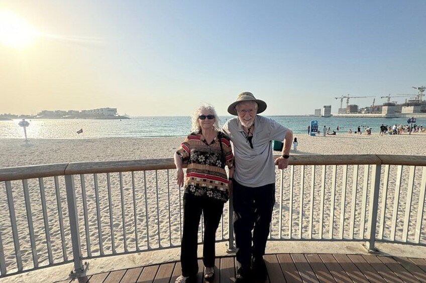 Two people standing on a wooden boardwalk with a beach and ocean in the background. 2