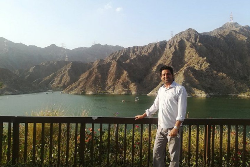 A person standing by a railing overlooking a lake with mountains in the background. 3