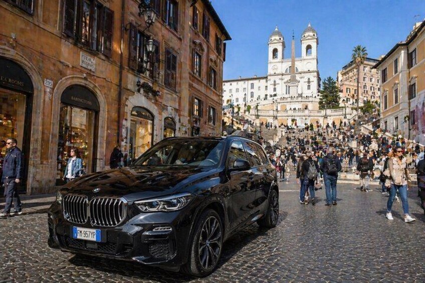 A black SUV parked on a cobblestone street with a crowd and a church in the background. 2
