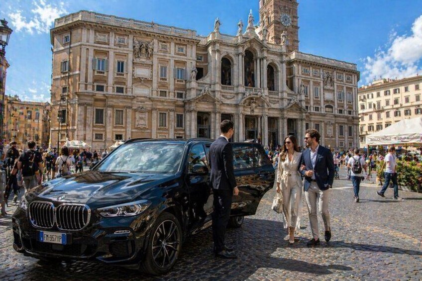 A black BMW SUV parked on a cobblestone street in front of a historic building with a clock tower. 4