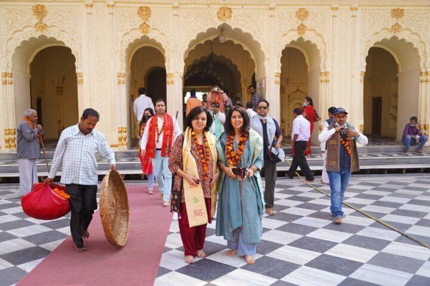 A group of people walking on a checkered floor with arches and a building in the background. 2