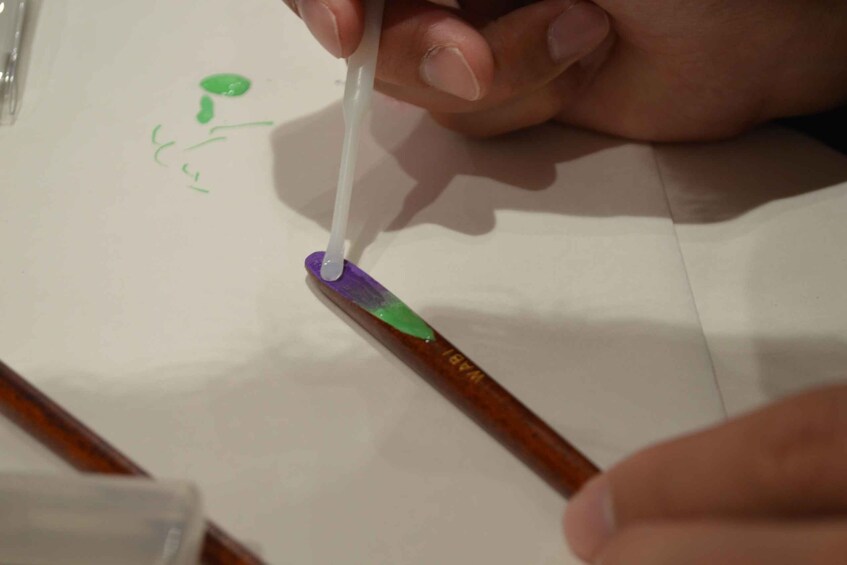 A hand holding a paintbrush applying purple paint to a white surface. 2