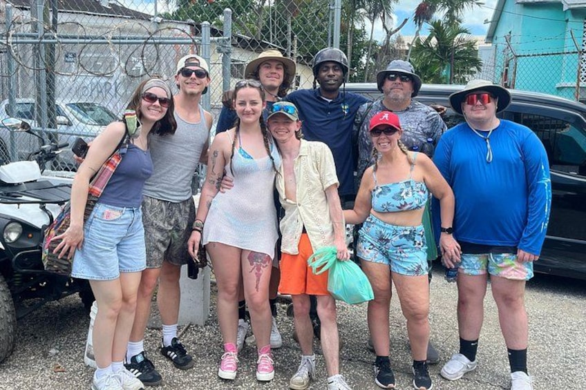 Un grupo de personas posando para una foto al aire libre, con un vehículo y una cerca de fondo. 4