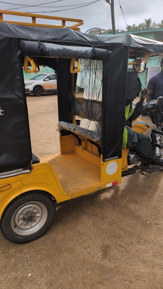 A yellow auto-rickshaw parked on a dirt road with a black tarp covering the back. 4