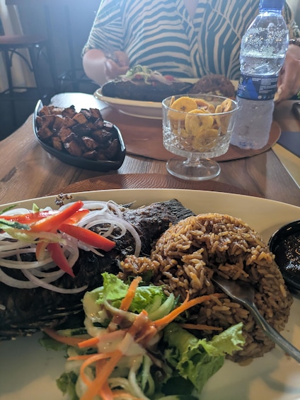 A plate of food with rice, vegetables, and a fish dish, with a water bottle and a bowl of chips on the table. 5