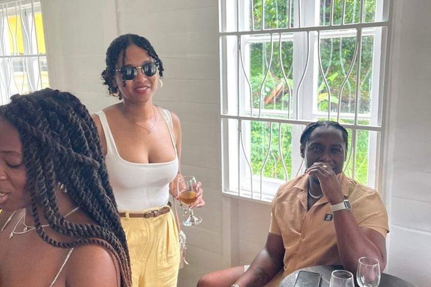 Three people sitting at a table with drinks, a window with metal bars, and greenery outside. 3
