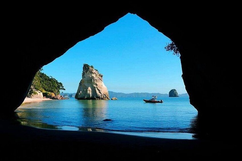 A cave opening to a coastal scene with a prominent rock formation, calm water, and a small boat. 2