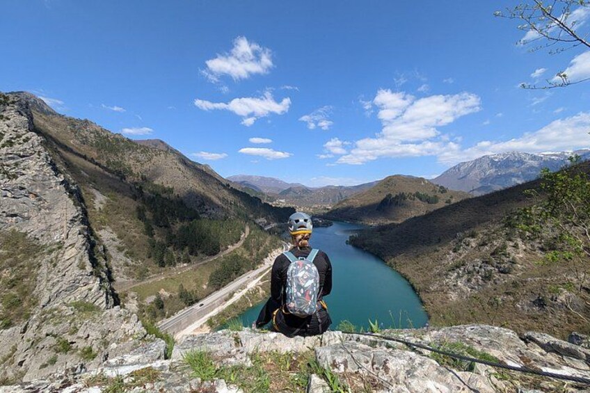A person sitting on a rocky ledge overlooking a turquoise river with mountains in the background. 3