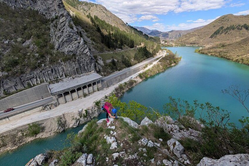 A river with a dam, rocky terrain, and a person in a red shirt and blue cap. 2
