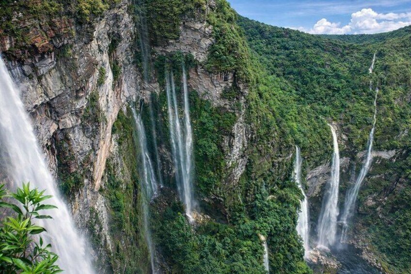Ein mehrstufiger Wasserfall stürzt über eine steile Felswand, umgeben von üppiger Vegetation. 2