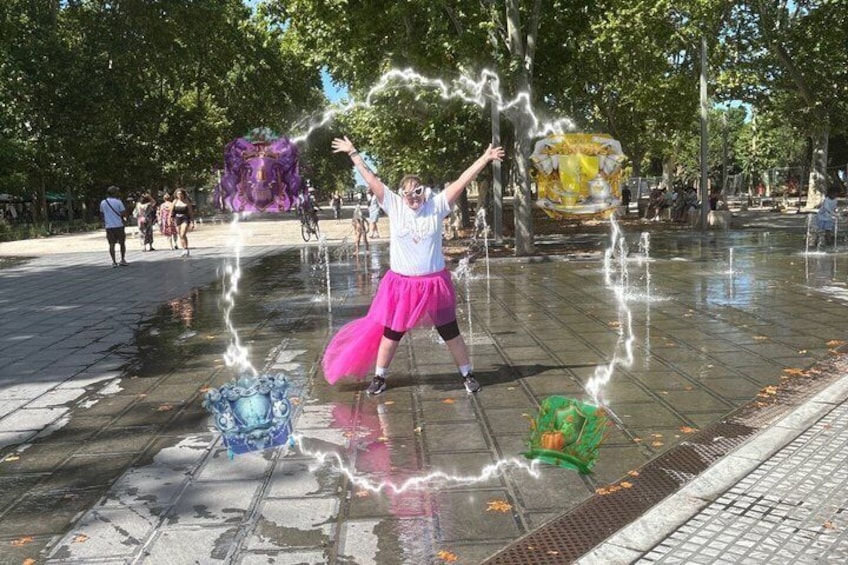 A person in a white shirt and pink skirt performing a water fountain act in a public square. 5
