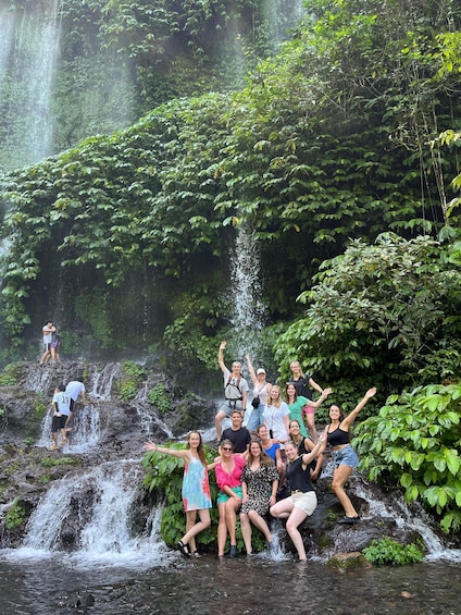 A group of people posing in front of a waterfall surrounded by lush greenery. 1