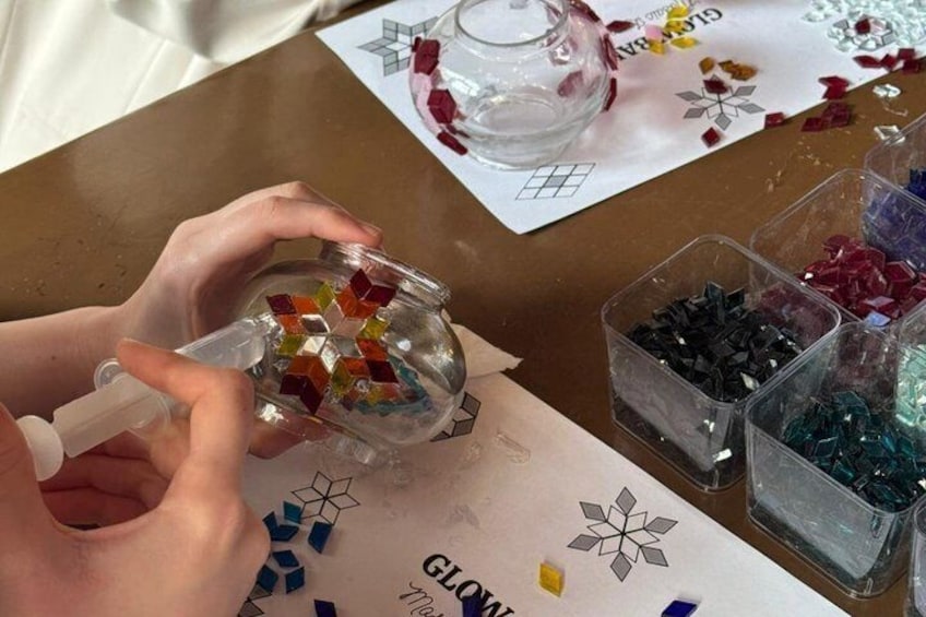 Des mains assemblent un bocal en verre avec des morceaux de mosaïque aux couleurs vives. 3