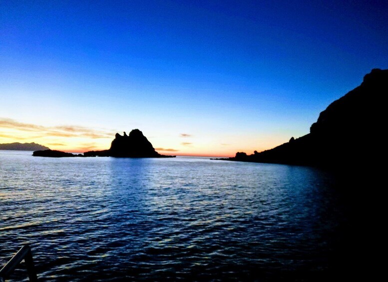 A coastal landscape with a prominent rock formation silhouetted against a sunset sky. 5