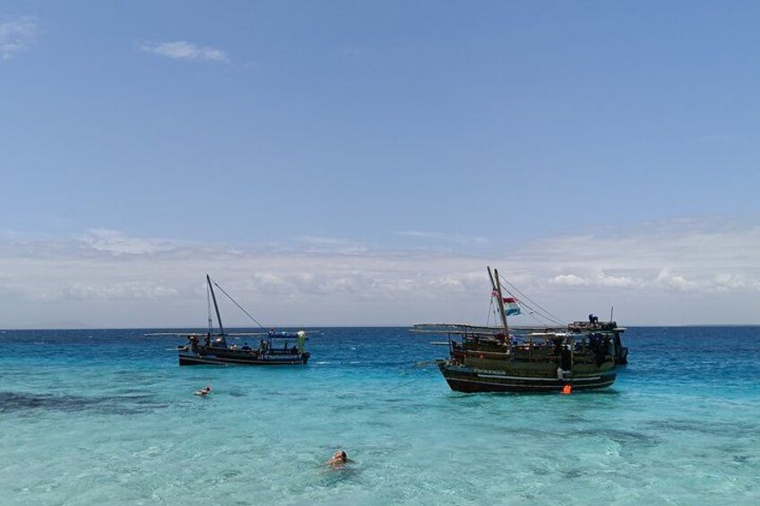 Deux bateaux sur une eau turquoise et limpide, avec un nageur au premier plan. 2