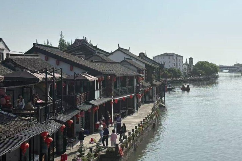 Une promenade le long de la rivière, bordée de bâtiments traditionnels, un pont visible au loin et une surface d’eau calme. 4