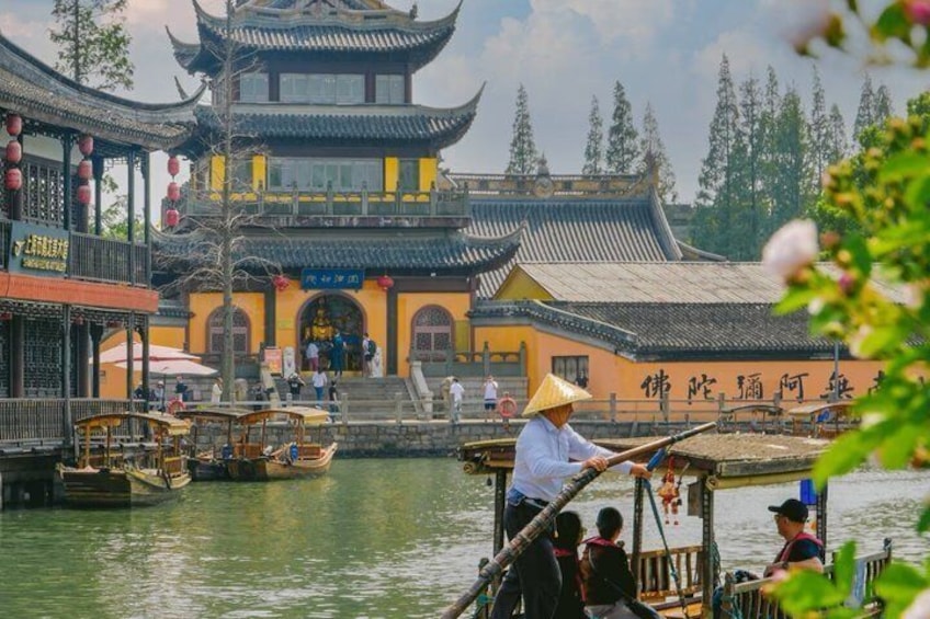 Un bâtiment traditionnel chinois, doté d’un toit à plusieurs niveaux, bordé d’un canal où naviguent des bateaux, et où l’on peut voir des personnes vêtues de costumes traditionnels. 1