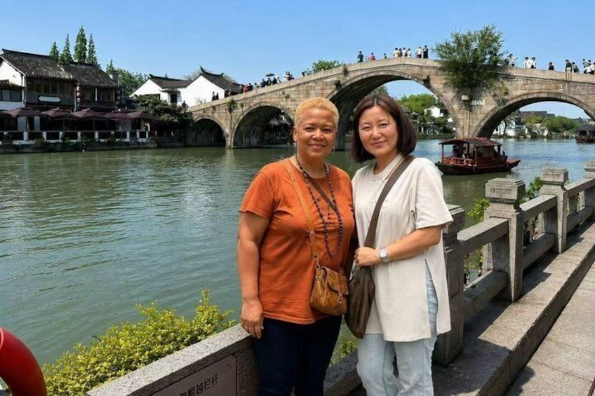 Deux personnes se tiennent près d’une rivière, avec un pont de pierre en arrière-plan. 2