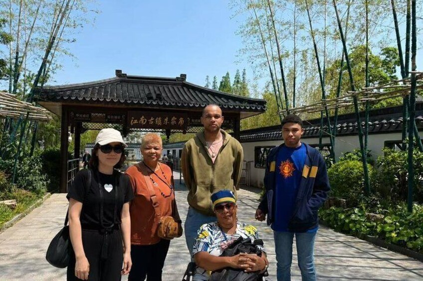 Un groupe de personnes se tient devant un pavillon traditionnel doté d’un toit en tuiles, entouré de verdure. 3