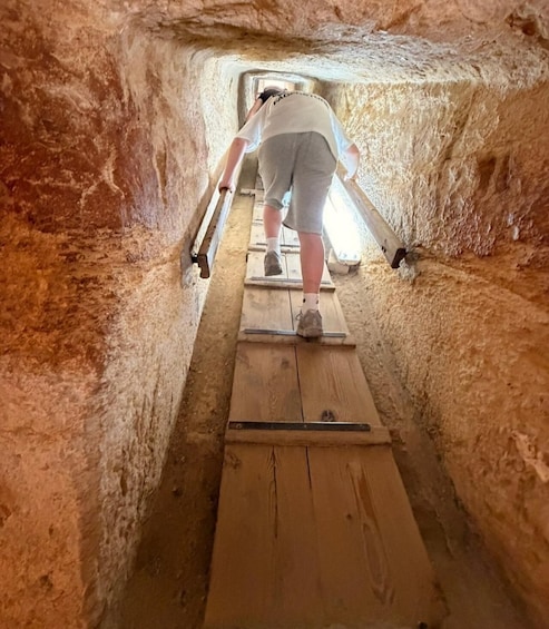 A person climbing a wooden ladder in a narrow, rocky passageway. 3