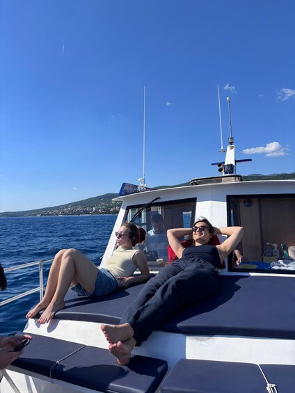 Two people relaxing on a boat with a clear blue sky and a distant shoreline. 2