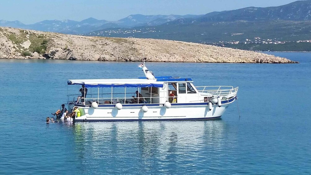 A boat with passengers on a calm lake, surrounded by mountains and a rocky shoreline. 1