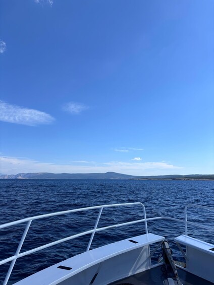 A boat's railing, calm sea, and distant mountains under a clear sky. 3