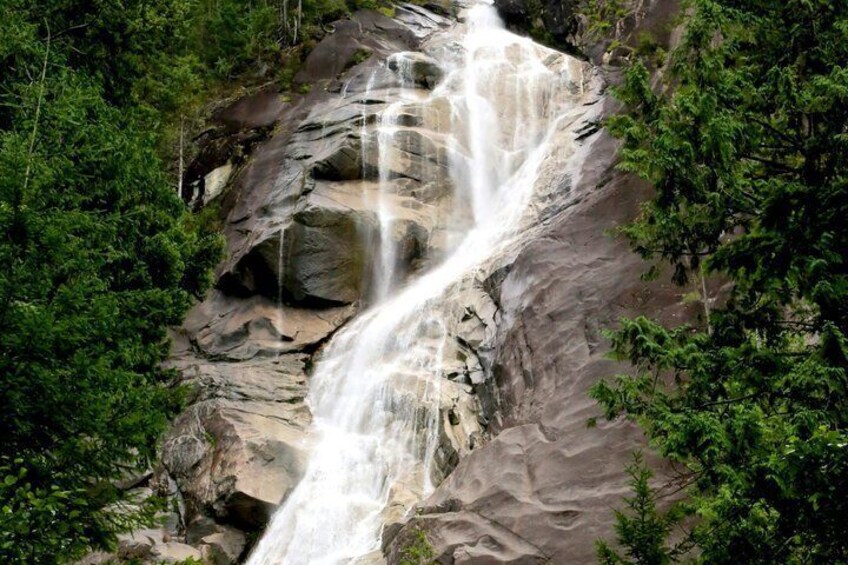 A waterfall cascading over a rocky cliff surrounded by dense green foliage. 3