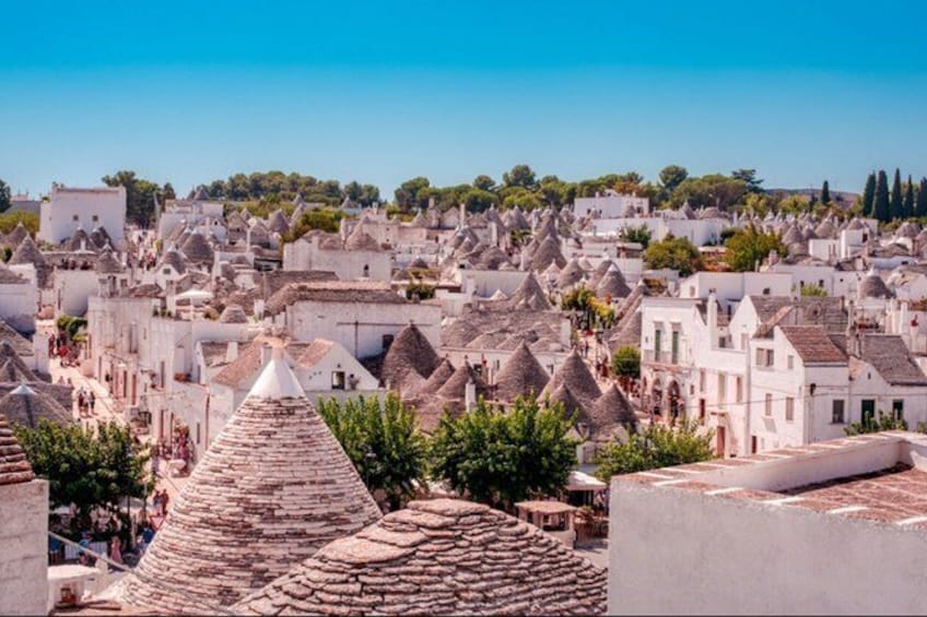 A town with white buildings and conical roofs, a clear blue sky, and trees in the background. 3
