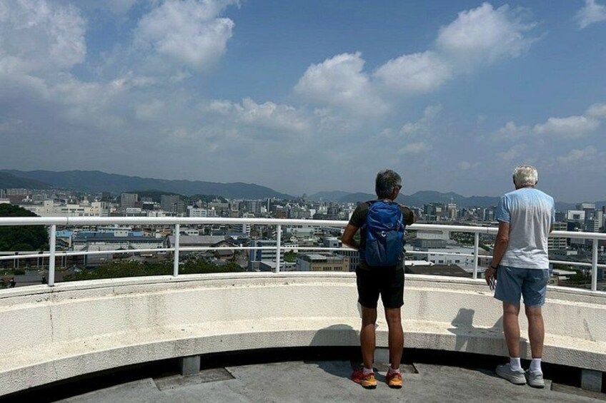 Two people standing on a bridge overlooking a cityscape with mountains in the distance. 5