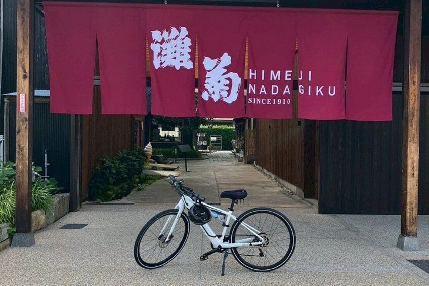 A bicycle parked in front of a building with a red banner displaying Japanese characters and the text 'Himeji Nada Giku Since 1910'. 4