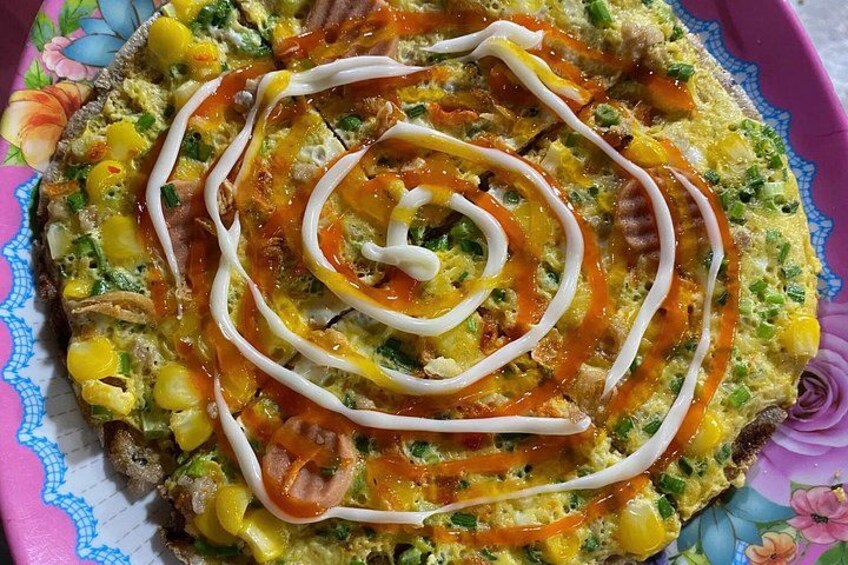 Una tortilla de verduras colorida con un dibujo espiral de salsa sobre un plato estampado con motivos florales. 2