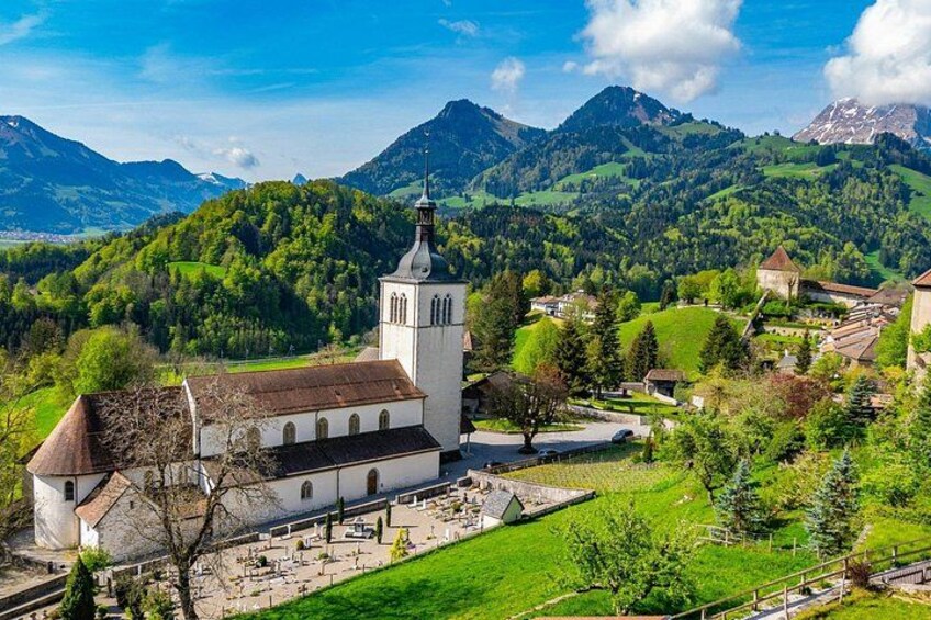 Une église dotée d’un clocher, entourée de collines et de montagnes verdoyantes. 2