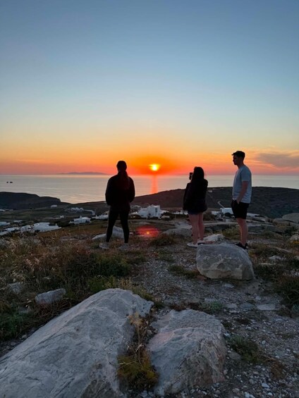 Three people standing on a rocky outcrop overlooking a sunset over the sea. 1