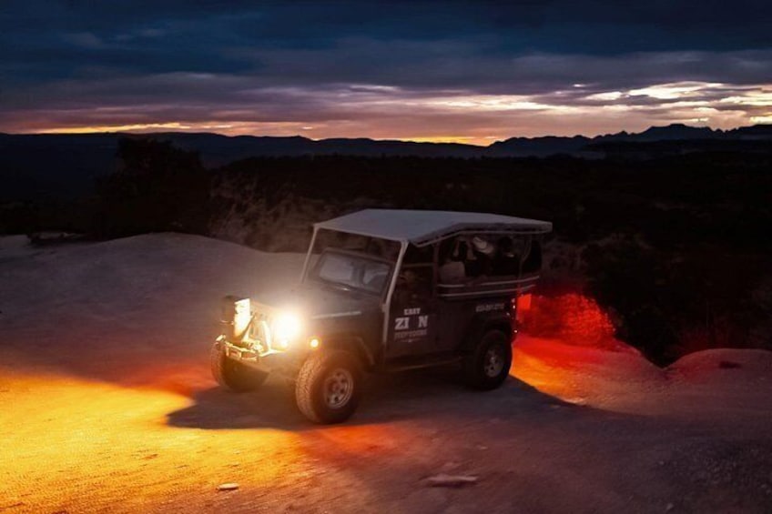 A vehicle on a dirt road at dusk with a mountainous backdrop. 3