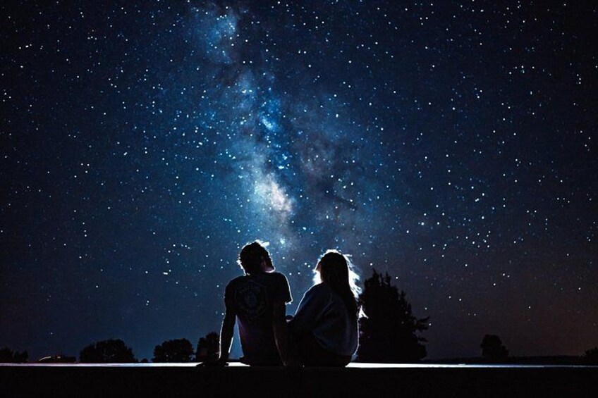 Dos personas sentadas bajo un cielo estrellado, con la Vía Láctea visible. 3
