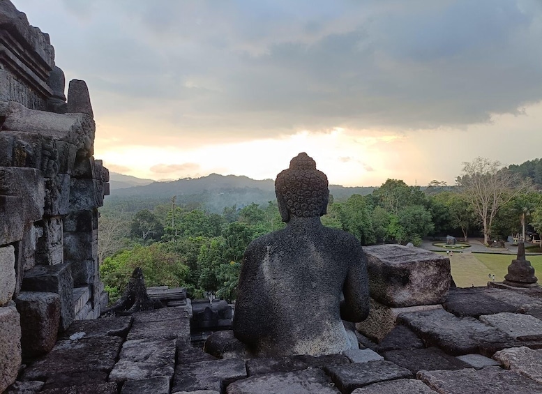 A stone Buddha statue overlooking a lush landscape with mountains in the distance. 2
