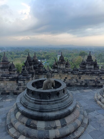A stone Buddha statue in a circular niche surrounded by tiered stone structures, overlooking a lush landscape. 4