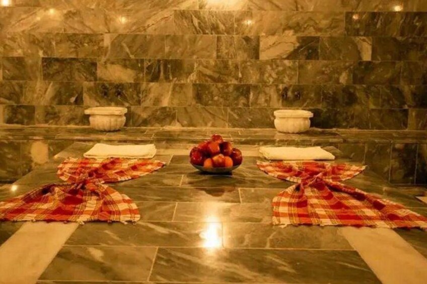 Un spa con pared de mármol, un cuenco de fruta y toallas a cuadros blancos y rojos en el suelo. 2
