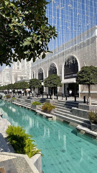 A pool with clear water, surrounded by trees and a building with arched windows. 1