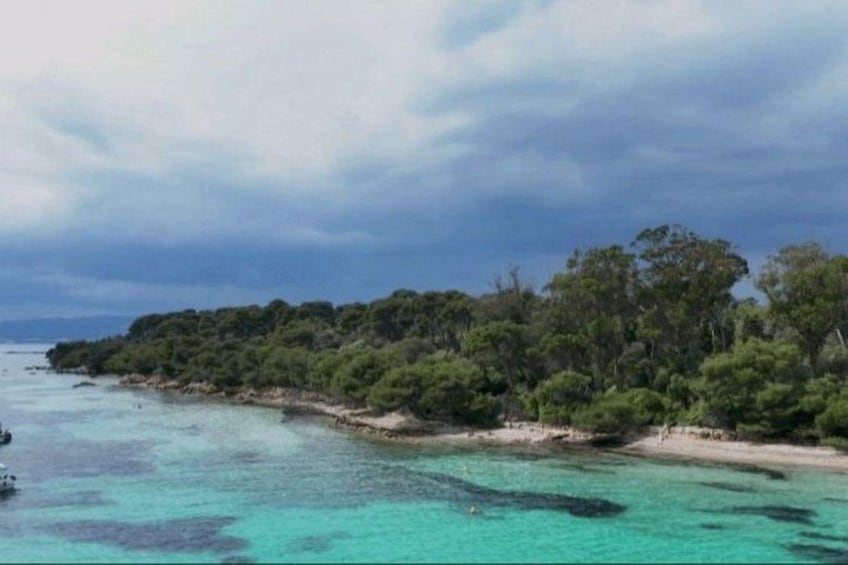 A coastal landscape with clear turquoise waters, a sandy beach, and dense green vegetation. 2