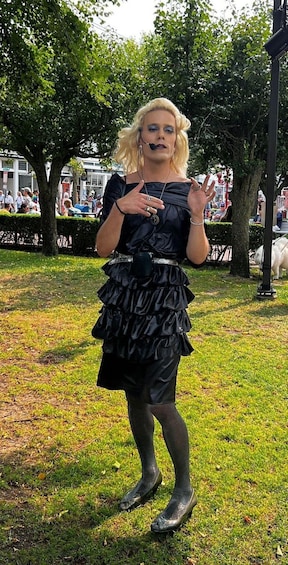 A person in a black dress with ruffles, standing on grass with trees and a white dog in the background. 3