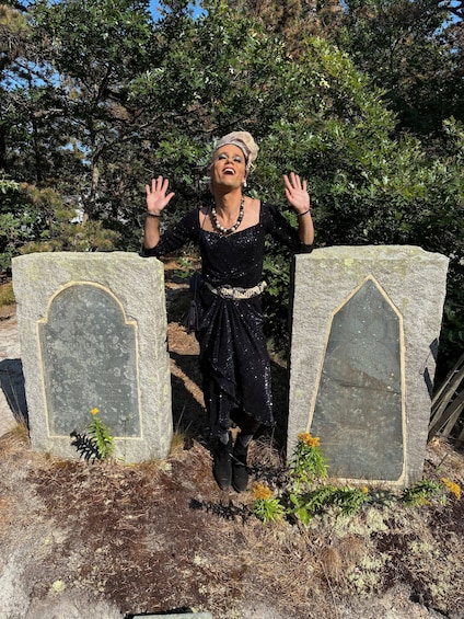 A person standing between two tombstones in a graveyard with trees in the background. 1