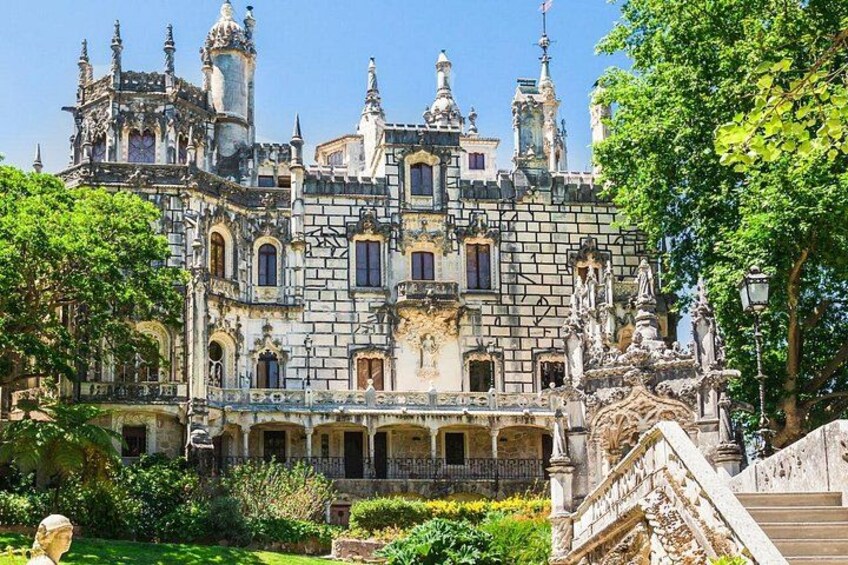 Un edificio storico con architettura elaborata, una scalinata monumentale e una vegetazione rigogliosa. 4