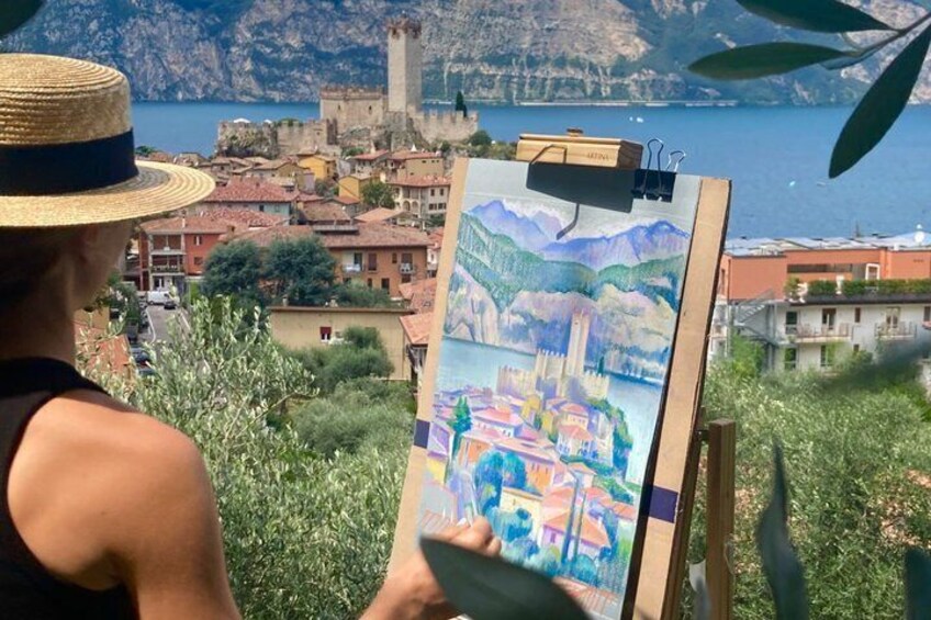 A person painting a landscape with a coastal town and mountains in the background. 4