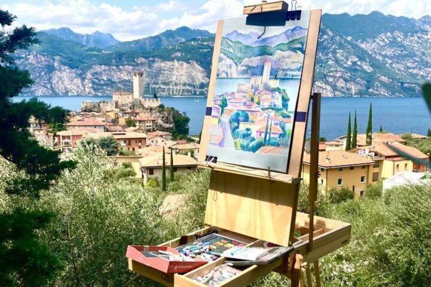An easel with a painting of a coastal village, surrounded by lush greenery and mountains. 2