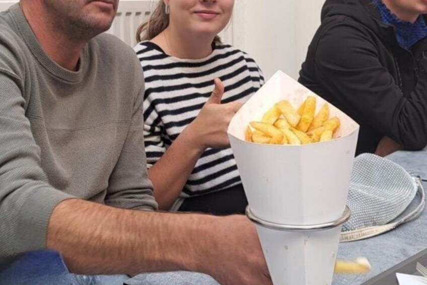 Three people sitting at a table with a white paper cup containing fries. 4
