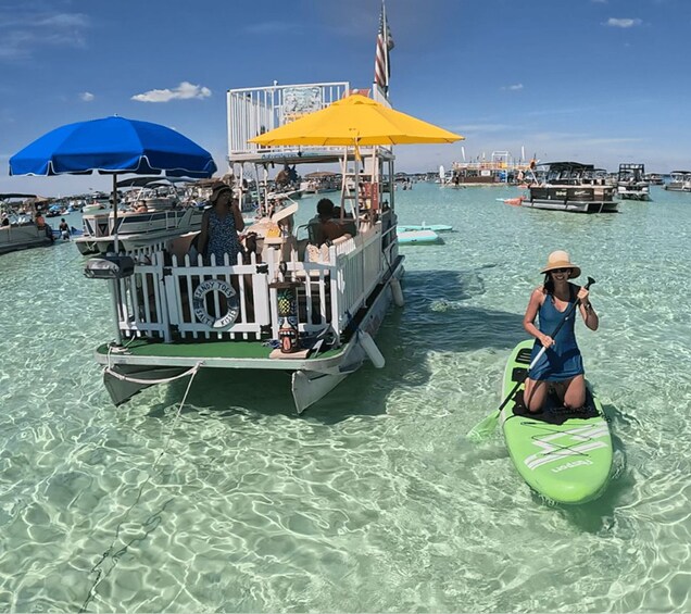 A boat with a white fence and a yellow umbrella, a person in a green kayak, and clear shallow water. 3